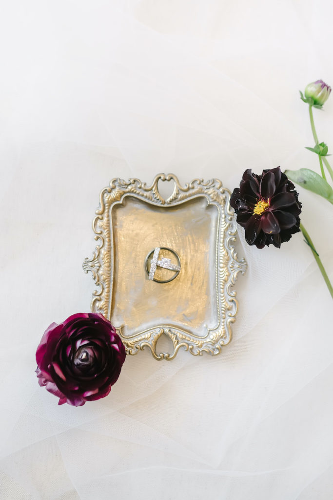 Diamond wedding bands styled on a gold tray with burgundy floral accents