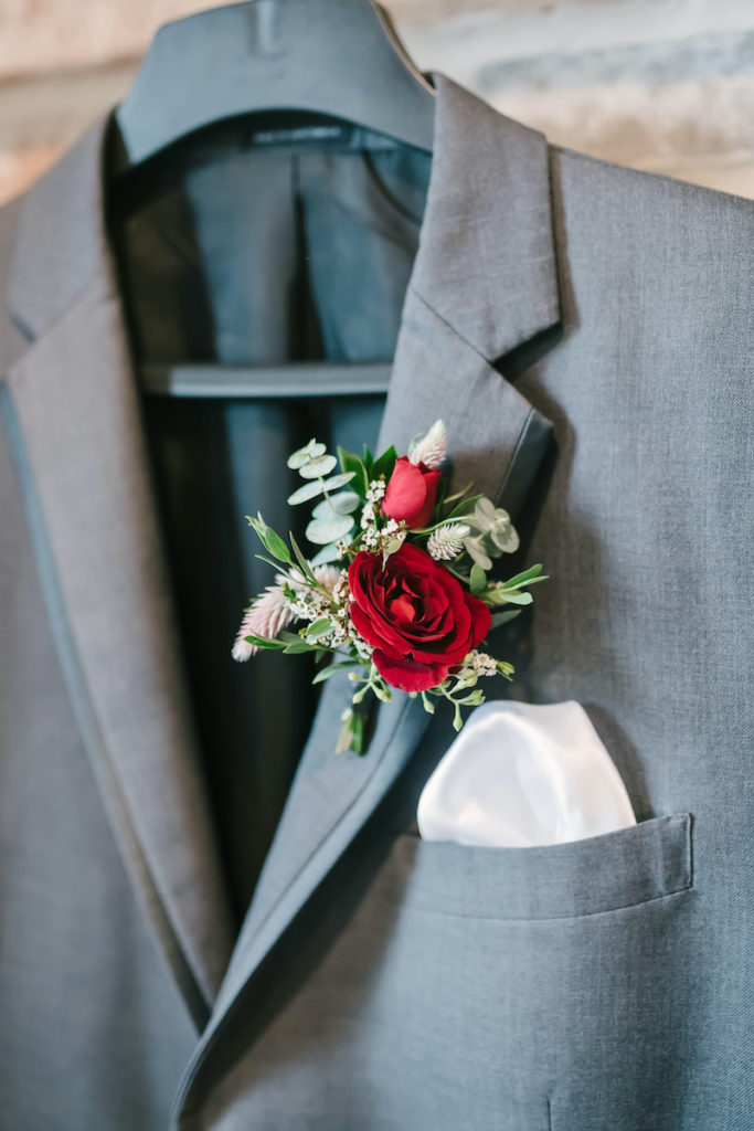 Red floral boutonnière created by Willow Lane Floral pinned to the grooms suit jacket