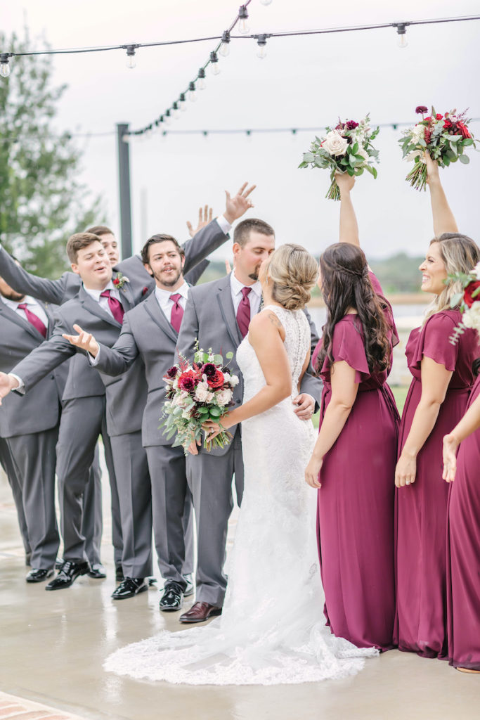 Wedding party cheers as the groom steals a kiss from his new wife