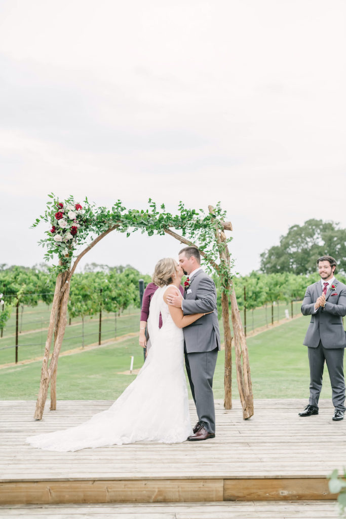 Bride and groom kiss under the floral arbor at the ceremony site at the Weinberg at Wixon Valley