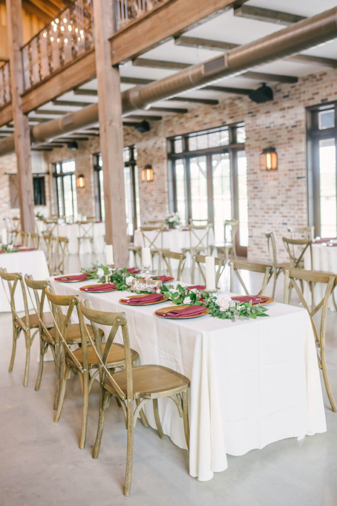 Cross back wooden chairs with set at the white tables with gold charger plates