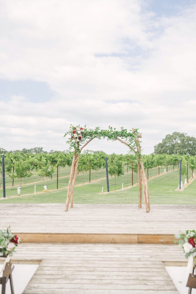 Rustic wooden arch adorned with greenery and florals at the outdoor ceremony site