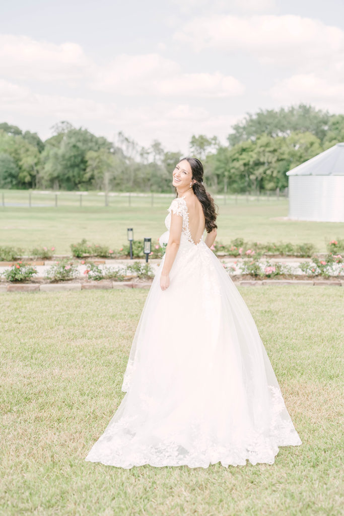 Beautiful long plunging back of white sheer and lace wedding dress with full skirt by Christina Elliot Photography in Houston, TX. alvin tx brazoria county wedding photographer back of wedding dress ideas low cut wedding dresses backless wedding dresses plunging neckline wedding dresses lace and sheer wedding dresses still waters ranch event venue #houstontexasphotographer #alvintxweddingphotographer #texasweddingphotography #outdoorbridalformals #bridalphotography