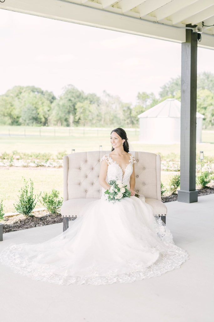 Beautiful bride posed for formals on a cream tufted love seat at Still Waters Ranch Event Venue in Houston, TX. alvin texas bridal locations in texas outdoor bridal locations houston wedding photographer props for bridals pose ideas for bridals chair poses for bridals lace wedding dress inspo brazoria county wedding photographer #houstontexasphotographer #alvintxweddingphotographer #texasweddingphotography #outdoorbridalformals #bridalphotography