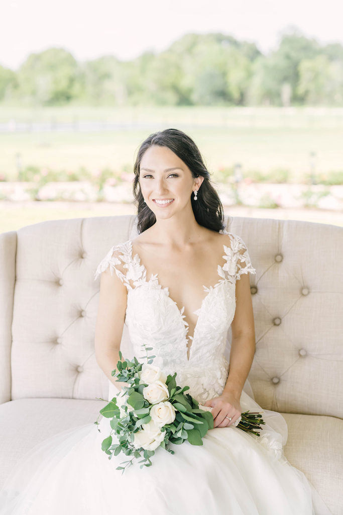 Bride in sweetheart neckline dress with v-neck and sheer with lace sitting on tufted loveseat chair by Christina Elliot Photography in Houston, TX. alvin texas still waters ranch event venue alvin wedding photographer brazoria county outdoor bridals chair prop for bridals sitting poses for bridals sweetheart neckline for wedding dress #houstontexasphotographer #alvintxweddingphotographer #texasweddingphotography #outdoorbridalformals #bridalphotography