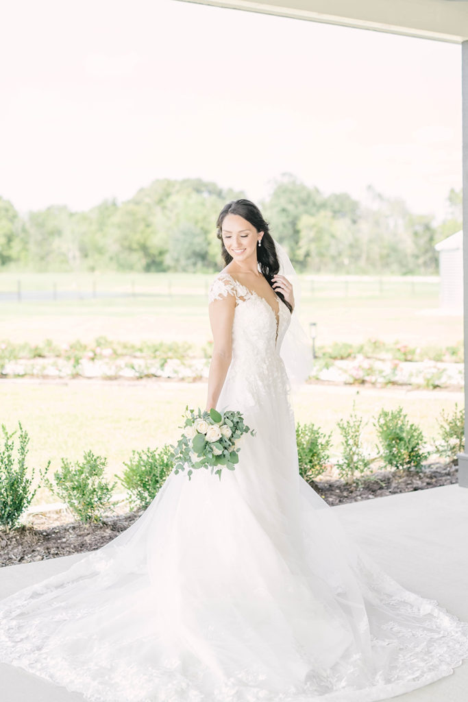 Elegant bride with white lace wedding dress and white and green wedding bouquet with hair pulled half back by Christina Elliot Photography in Houston, TX. alvin texas wedding dress outfit inspo lace wedding dresses hair inspo for wedding simple hair styles for wedding flower bouquet ideas white wedding bouquets white wedding colors #houstontexasphotographer #alvintxweddingphotographer #texasweddingphotography #outdoorbridalformals #bridalphotography