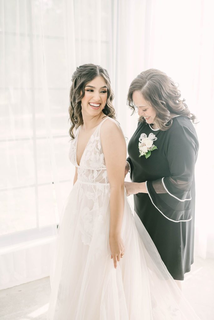 Mother and bride getting ready wearing lacy cream wedding dress and black dress with white detail flowing sleeves by Christina Elliot Photography in Houston, TX. greenhouse wedding mother of the bride outfit inspo colors for mother of bride houston wedding photographer the oak atelier woodlands tx mother and daughter wedding poses #houstontexasphotographer #houstonweddingphotographer #texasweddingphotography #greenhousewedding #outdoorweddinginspo