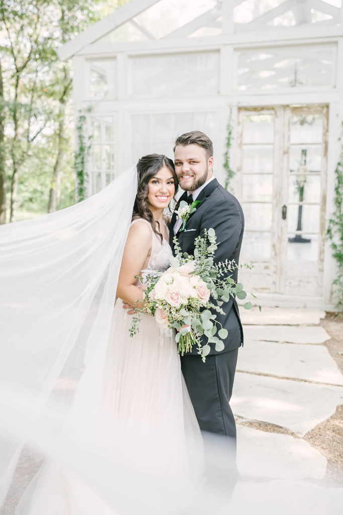 Bride and groom formals at greenhouse location with green vines floral doing first look moment in Houston, TX by Christina Elliot Photography. first look photography bride and groom first look greenhouse wedding vines and greenery decor for wedding the oak atelier woodlands houston wedding photographer cream wedding dress black tuxedo for groom #houstontexasphotographer #houstonweddingphotographer #texasweddingphotography #greenhousewedding #outdoorweddinginspo