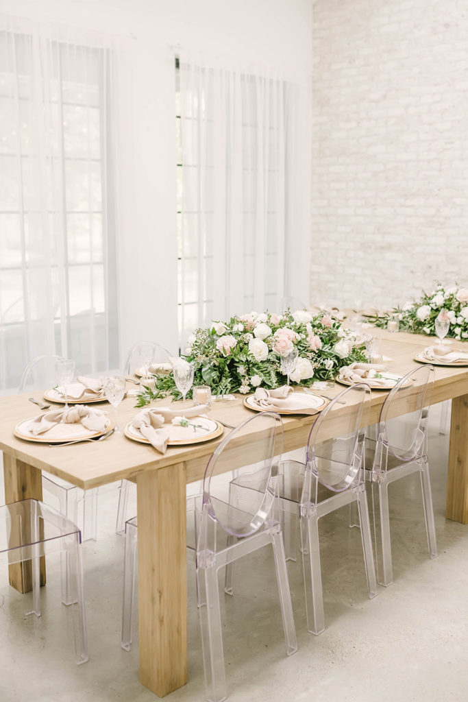 Beautiful table setting for wedding dinner with clear plastic glass chairs and light wood table with flower and leaf garland runner in Houston, TX by Christina Elliot Photography. wedding dinner inspo ideas for wedding dinner table setting clear chairs glass chairs for wedding table runners for wedding floral table runner greenhouse #houstontexasphotographer #houstonweddingphotographer #texasweddingphotography #greenhousewedding #outdoorweddinginspo