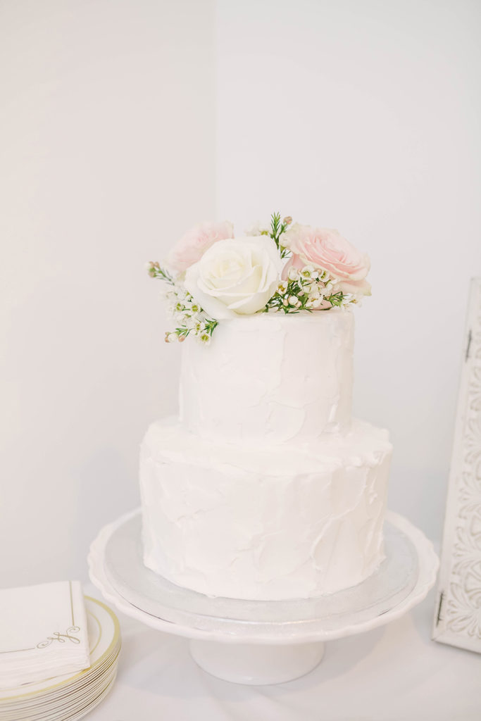 Two-tier simple and elegant white wedding cake with pink and white flowers on top by Christina Elliot Photography in Houston, TX. wedding cake inspo white wedding cakes simple wedding cakes wedding cakes with flowers how to style a wedding cake greenhouse wedding the oak atelier woodlands houston wedding photography white wedding inspo #houstontexasphotographer #houstonweddingphotographer #texasweddingphotography #greenhousewedding #outdoorweddinginspo