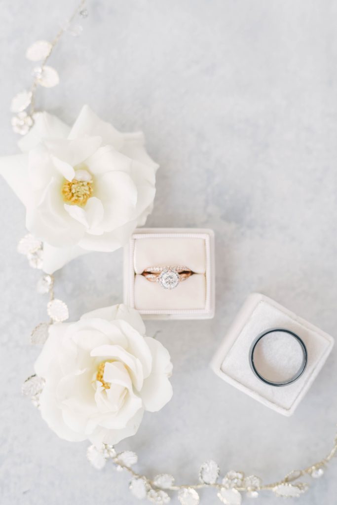 Diamond Wedding ring styled in pale pink ring box surrounded by white flowers and gold hairpiece