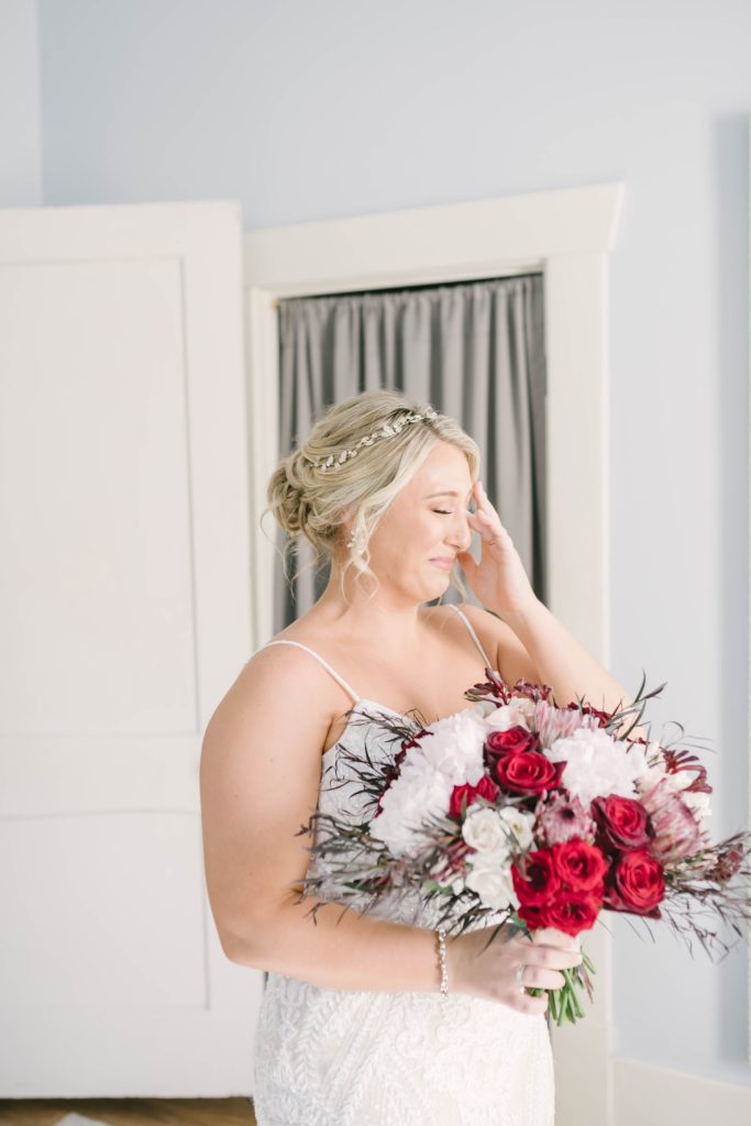 A bride takes a moment as she gets a little teary eyed before her wedding ceremony captured by Christina Elliott Photography. Bridal bouquet inspiration summer weddings gorgeous wedding color ideas deep red lace wedding dress inspo bridal hair updo ideas