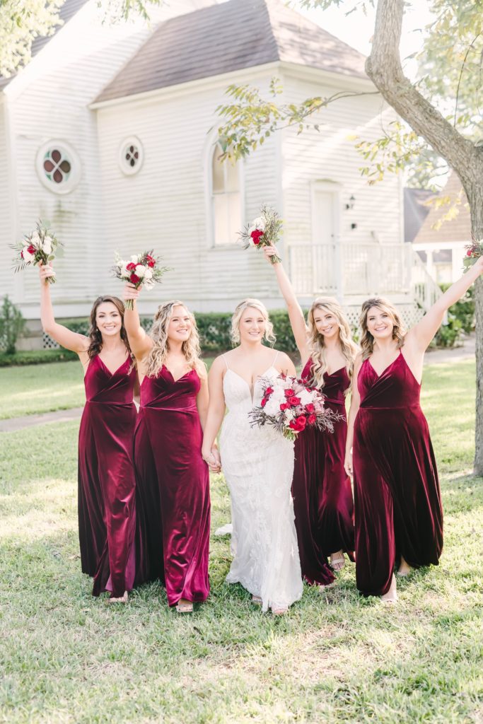 Bride with her bridesmaids smiling and laughing as they walk towards the camera taken before her wedding ceremony. Texas brides Christina Elliot wedding photography Texas based matching bridesmaid dresses deep red wedding colors sleeveless bridesmaid dresses