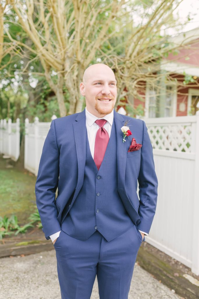 Handsome photo of the groom smiling in his wedding suit captured by Christina Elliot Photography at Butler’s Courtyard. Texas weddings photos of the groom summer wedding attire navy blue suit men’s single photo pose ideas masculine poses for grooms