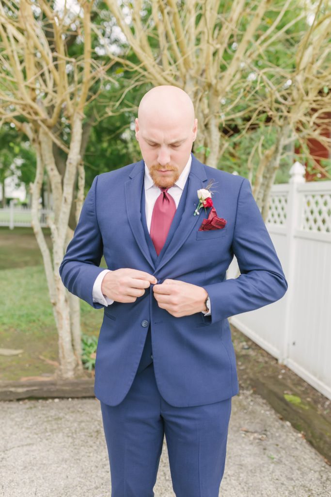 Dashing image of the groom adjusting his suit lapel before his wedding ceremony at Butler’s Courtyard in League City, Texas. Wedding day photos individual shots masculine poses for grooms and groomsmen summer weddings navy blue suit inspo #houstonweddingphotographer #christinaelliotphotography #weddingphotographer