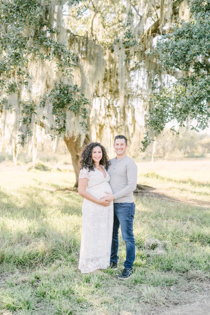 During this Houston, Texas maternity session, Christina Elliott Photography captures this expectant couple posing happily beneath a shade tree. Houston Texas maternity photographer white v-neck maxi lace maternity dress #HoustonMaternityPhotographer #HoustonCouplesPhotographer #HoustonPhotographer #MaternitySession #MaternityDresses #ChristinaElliottPhotography #HoustonFamilyPhotographer #Pregnant #BabyBump #WereExpecting