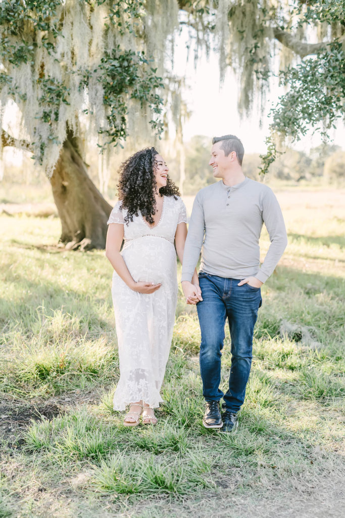 Christina Elliott Photography captures this expectant couple link arms and smile lovingly at one another during this maternity session in Houston, Texas. Houston maternity photographer white cap sleeve lace maxi dress couple maternity poses #HoustonMaternityPhotographer #HoustonCouplesPhotographer #HoustonPhotographer #MaternitySession #MaternityDresses #ChristinaElliottPhotography #HoustonFamilyPhotographer #Pregnant #BabyBump #WereExpecting