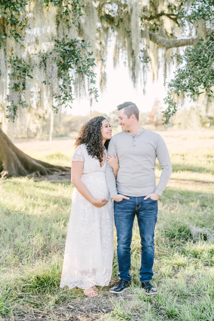 Christina Elliott Photography captures this expectant couple link arms and smile lovingly at one another during this maternity session in Houston, Texas. Houston maternity photographer white cap sleeve lace maxi dress couple maternity poses #HoustonMaternityPhotographer #HoustonCouplesPhotographer #HoustonPhotographer #MaternitySession #MaternityDresses #ChristinaElliottPhotography #HoustonFamilyPhotographer #Pregnant #BabyBump #WereExpecting