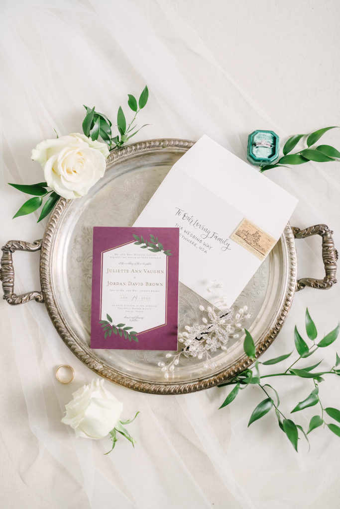 A beautiful shot of the wedding invitation to this barn style wedding in Alvin, Texas captured by Christina Elliot Photography. Wedding invitation inspo purple red invites greenery floral silver platter details houston texas wedding photographer Christina elliot photos #houstonweddingphotographer #texasphotographer #weddingdaydetails #barnstylewedding #stillwatersranch #alvintexasphotographer #weddingday #brideandgroom #texanwedding #htxwedding #countrywedding