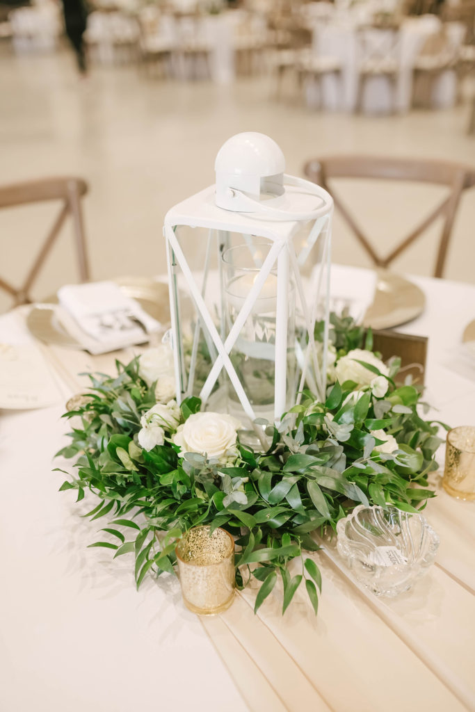 A stunning and elegant table centerpiece in this barn style wedding in Alvin, Texas captured by Christina Elliot Photography. Centerpiece wedding decor white lantern greenery decorations inspo gold candles white flower tablecloth table rustic wedding #houstonweddingphotographer #texasphotographer #weddingdaydetails #barnstylewedding #stillwatersranch #alvintexasphotographer #weddingday #brideandgroom #texanwedding #htxwedding #countrywedding
