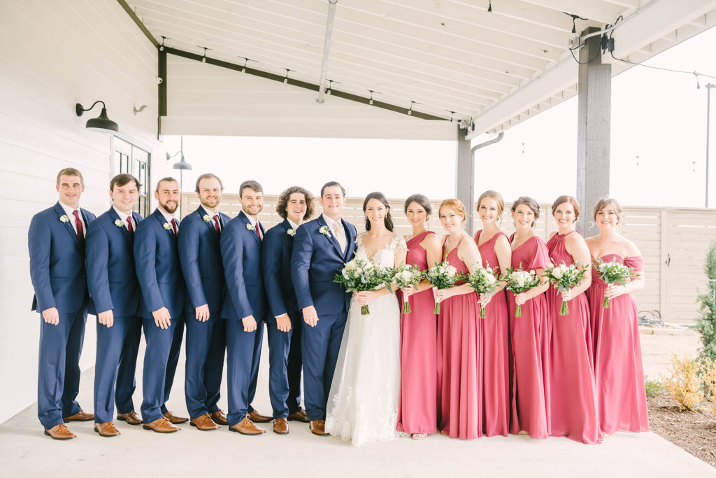 A beautiful shot of the wedding party and bride and groom before the ceremony in Houston, Texas with Christina Elliot Photography. bridesmaids groomsmen wedding party pink dress navy suit white dress bride and groom floral bouquets alvin texas wedding photographer barn style country inspiration #houstonweddingphotographer #texasphotographer #weddingdaydetails #barnstylewedding #stillwatersranch #alvintexasphotographer #weddingday #brideandgroom #texanwedding #htxwedding #countrywedding