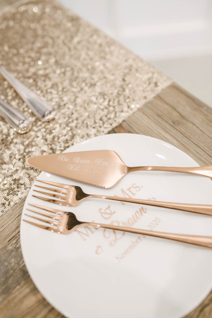A details shot of cutting the cake tools at a barn style wedding at Still Waters Ranch in Alvin, Texas captured by Christina Elliot Photography. Cutting the cake tradition rose gold fork cake slicer Mr and Mrs white plate wedding day details inspo texas photography #houstonweddingphotographer #texasphotographer #weddingdaydetails #barnstylewedding #stillwatersranch #alvintexasphotographer #weddingday #brideandgroom #texanwedding #htxwedding #countrywedding