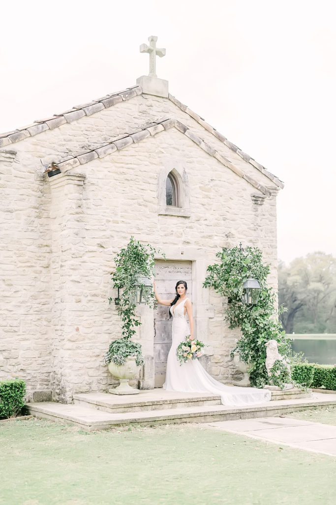 Bride posing with the stone chapel ceremony site at the Clubs of Houston Oaks