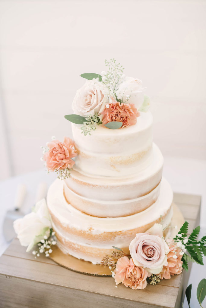 White almond naked cake adorned with blush and white roses and greenery.