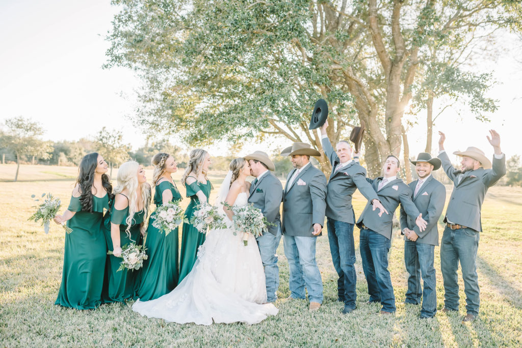 Full wedding party cheer as the bride and groom share a kiss at the Barn at Willowynn wedding venue in Santa Fe, TX.