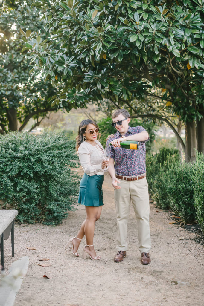 Pouring a drink to celebrate their engagement in Houston, Texas captured by Christina Elliot Photography. Playful outdoor engagement session houston texas wedding photography sunglasses semi formal attire inspo champagne glass flutes she said yes teal green skirt button up shirt details inspiration #houstonweddingphotographer #engagementpics #houstonphotographer #engagementphotos #shesaidyes #texasphotographer #photoinspiration #weddingphotography #houstonphotographer