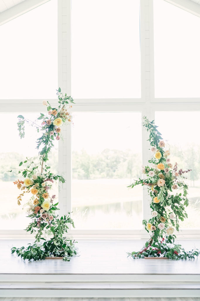Asymmetrical floral arch in white shiplap wedding venue chapel at the Farmhouse Wedding venue created by Jackie Trejo Floral Design.
