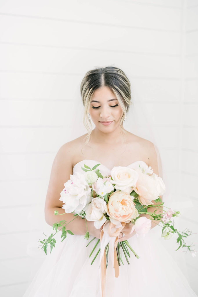 Bride in the white shiplap chapel at the Farmhouse wedding venue holding fluffy floral bouquet by Jackie Trejo Floral Design captured by Christina Elliott Photography.