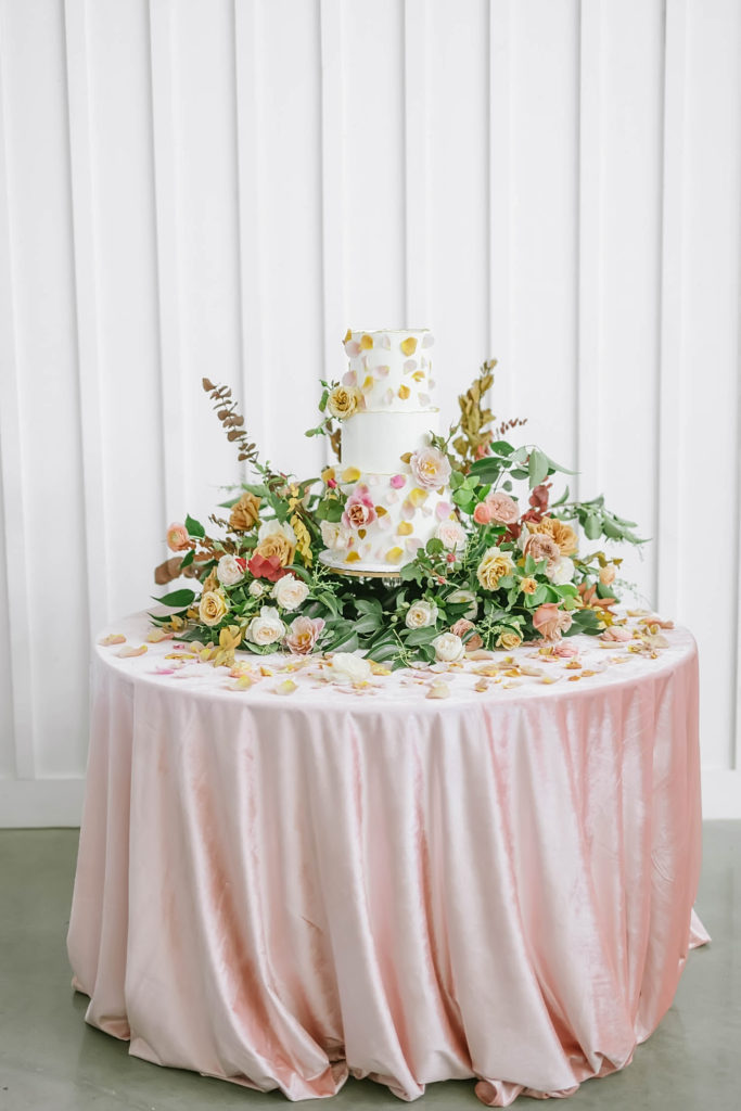 Stunning cake table with three tier wedding cake with floral accents and blush velvet table covering. #caketableinspo