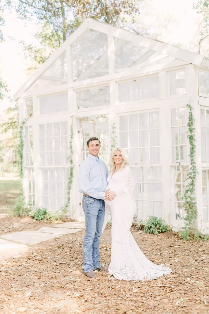 Expecting couple posed in front of the willow greenhouse at the Oak Atelier in a stunning white crochet maternity gown by Christina Elliott Photography. cowboy father maternity fashion ideas pregnancy goals #christinaelliottphotography #christinaelliotmaternitysession #babybump #houstonmaternityphotographer #houstonmaternity #pregnancypic #houstonphotographylocations #materntiyoutfit #soontobeparents #babyontheway #houstonphotos #houstontexasmaternityphotographer #oakatelierphotos #conroetexas
