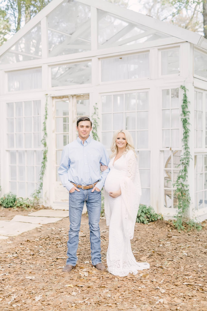 Outside a white glass window house Christina Elliott Photography captures a man and woman portrait during a fall maternity session in Conroe, Texas. light blue button up white crochet sleeves #christinaelliottphotography #christinaelliotmaternitysession #babybump #houstonmaternityphotographer #houstonmaternity #pregnancypic #houstonphotographylocations #materntiyoutfit #soontobeparents #babyontheway #houstonphotos #houstontexasmaternityphotographer #oakatelierphotos #conroetexas