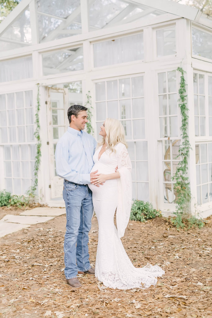Pregnant woman smiles at her husband in white crochet gown during maternity portraits with Christina Elliott Photography in Conroe, Texas. new parent love awaiting a baby sweet pregnancy pic #christinaelliottphotography #christinaelliotmaternitysession #babybump #houstonmaternityphotographer #houstonmaternity #pregnancypic #houstonphotographylocations #materntiyoutfit #soontobeparents #babyontheway #houstonphotos #houstontexasmaternityphotographer #oakatelierphotos #conroetexas