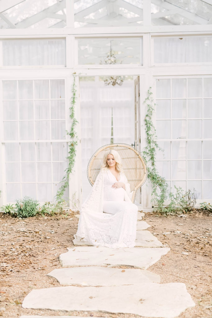 Christina Elliott Photography captures a goregous maternity shot of a blonde woman in a white boho dress sitting on a wicker chair outside in Houston Texas. outdoor maternity session boho style maternity #christinaelliottphotography #christinaelliotmaternitysession #babybump #houstonmaternityphotographer #houstonmaternity #pregnancypic #houstonphotographylocations #materntiyoutfit #soontobeparents #babyontheway #houstonphotos #houstontexasmaternityphotographer #oakatelierphotos #conroetexas
