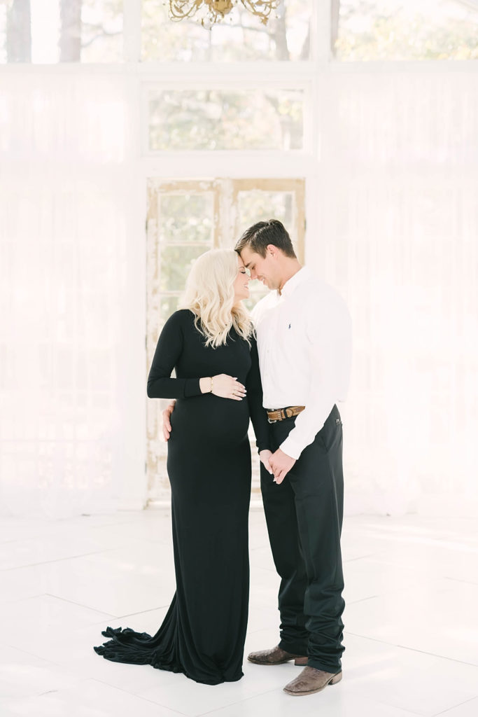 A couple with heads together and smiling in a white greenhouse awaiting the birth of their sweet baby by Christina Elliott Photography of Texas. smile away maternity photography beautiful pregnancy #christinaelliottphotography #christinaelliotmaternitysession #babybump #houstonmaternityphotographer #houstonmaternity #pregnancypic #houstonphotographylocations #materntiyoutfit #soontobeparents #babyontheway #houstonphotos #houstontexasmaternityphotographer #oakatelierphotos #conroetexas