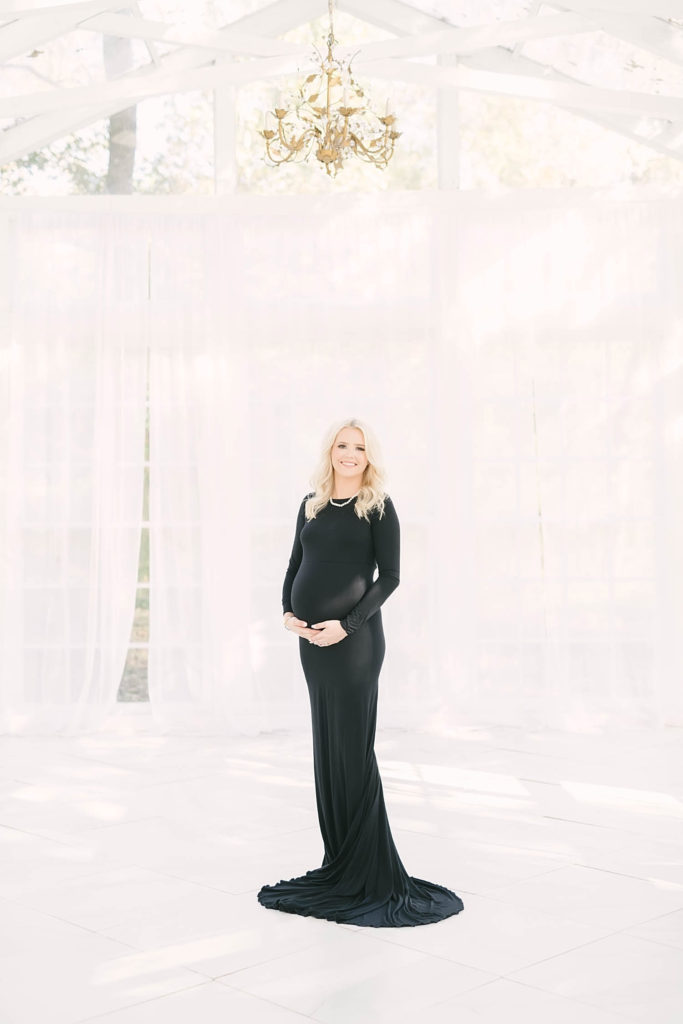 A stunning portrait of a mom to be holding her baby bump wearing a black fitted dress by Christina Elliott Photography. pregnancy photos blonde pregnant life maternity style ideas #christinaelliottphotography #christinaelliotmaternitysession #babybump #houstonmaternityphotographer #houstonmaternity #pregnancypic #houstonphotographylocations #materntiyoutfit #soontobeparents #babyontheway #houstonphotos #houstontexasmaternityphotographer #oakatelierphotos #conroetexas
