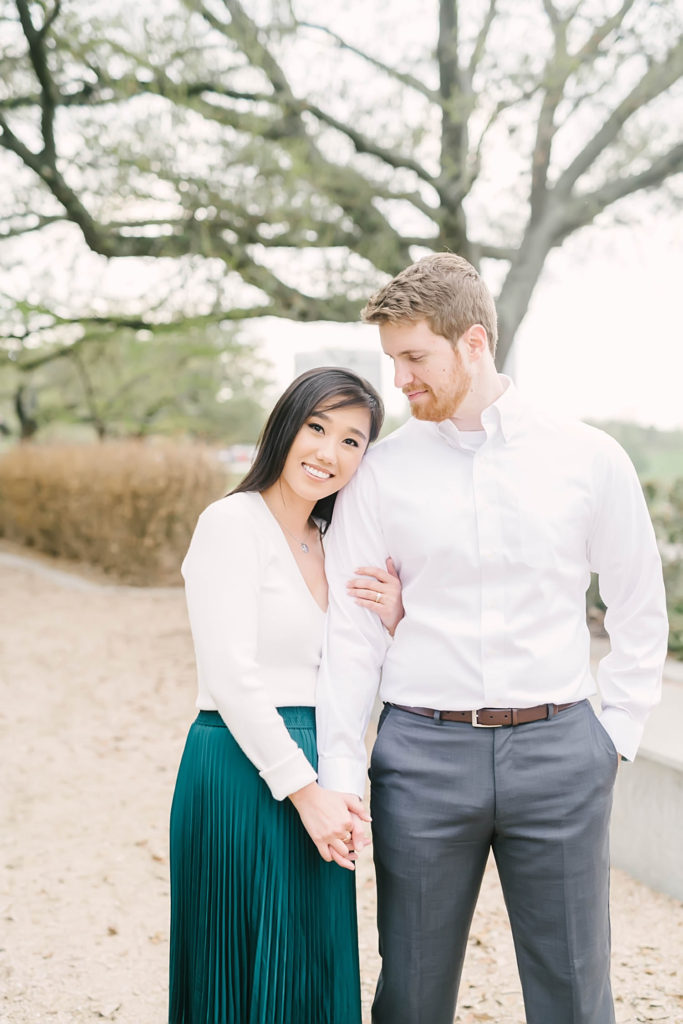 Groom in his gray slacks smiles down at his bride to be during their engagement photos at Eleanor Tinsley Park near Downtown Houston.