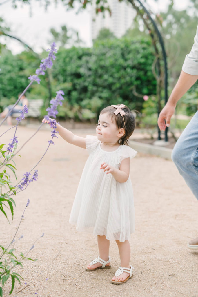 Baby girl plays with purple flowers in the Rose Gardens section at McGovern Centennial Gardens in the Houston Museum District.