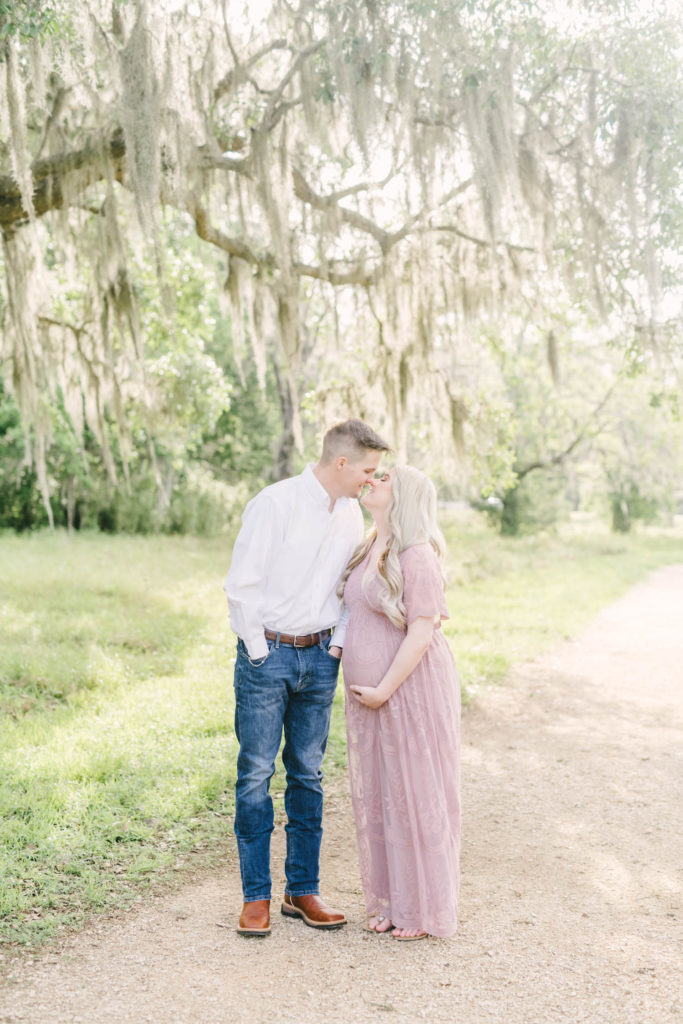 Christina Elliott Photography captures a couple kissing during their maternity portrait session at Brazos Bend State Park. lace pink dress southern pregnancy style elegent pregnancy attire #christinaeliottphotography #christinaelliotmaternity #brazosbendstatepark #houstonmaternityphotographer #parentstobe #babybumppicutes #houstonareaphotographer #professionalmaternityphotographer #houstonmaternity #preggo #pregnancyjournal #texasmaternityphotographer