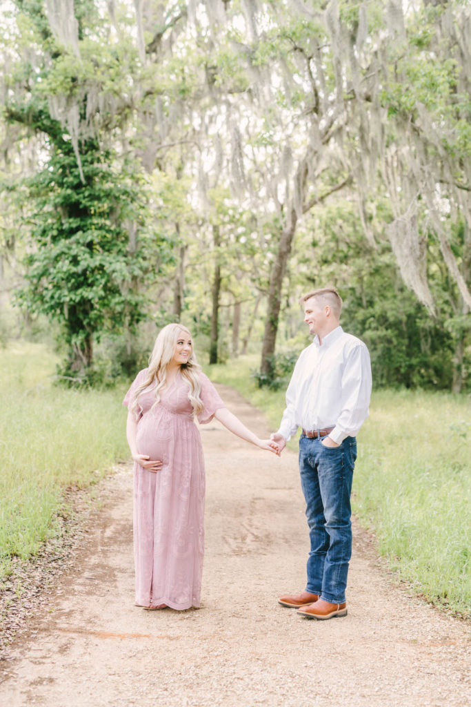 Young husband and wife hold hands and smile lovingly at each other in Brazos Bend State Park for their maternity session with Christina Elliott Photography. months pregnant pregnancy poses cowboy man style baby on the way pic #christinaeliottphotography #christinaelliotmaternity #brazosbendstatepark #houstonmaternityphotographer #parentstobe #babybumppicutes #houstonareaphotographer #professionalmaternityphotographer #houstonmaternity #preggo #pregnancyjournal #texasmaternityphotographer