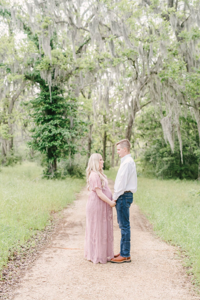 Couple holds hands on a gravel pathway in Brazos Bend State Park for their maternity portrait session with Christina Elliott Photography. hand holding couple country roads picture southern momma #christinaeliottphotography #christinaelliotmaternity #brazosbendstatepark #houstonmaternityphotographer #parentstobe #babybumpicutes #houstonareaphotographer #professionalmaternityphotographer #houstonmaternity #preggo #pregnancyjournal #texasmaternityphotographer