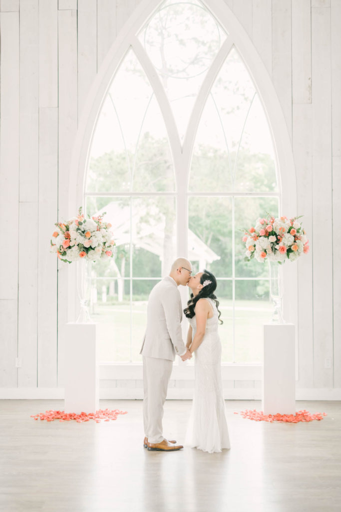 Couple kisses after a wedding ceremony in from on a white vintage barn window in Houston Texas by Christina Elliott Photography. couple kissing after ceremony vintage barn window til death do we part wedding details #christinaelliotphoto #christinaelliotphotography #christinaelliotelopements #elopementphotographer #wallisvillewedding #houstontexaswedding #houstonweddingphotographer #trinityfarmhouse #texaselopements #elopement #springwedding