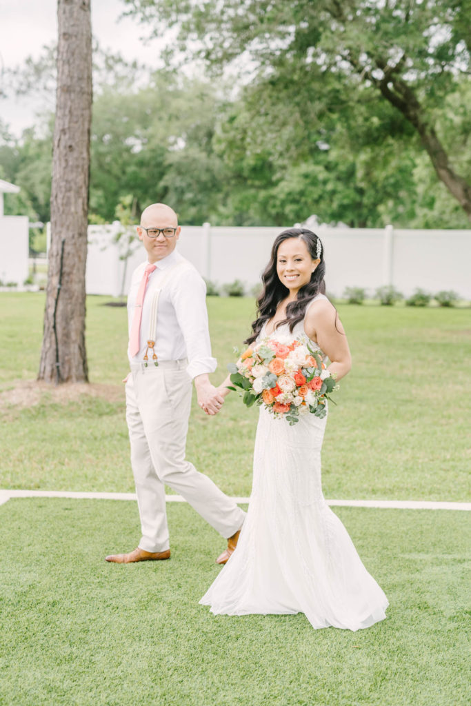 Houston area wedding photographer captures an Asian couple on their big day holding hands and walking on green grass with classy attire by Christina Elliott Photography. classy wedding attire spring floral bouquet springtime wedding #christinaelliotphoto #christinaelliotphotography #christinaelliotelopements #elopementphotographer #wallisvillewedding #houstontexaswedding #houstonweddingphotographer #trinityfarmhouse #texaselopements #elopement #springwedding