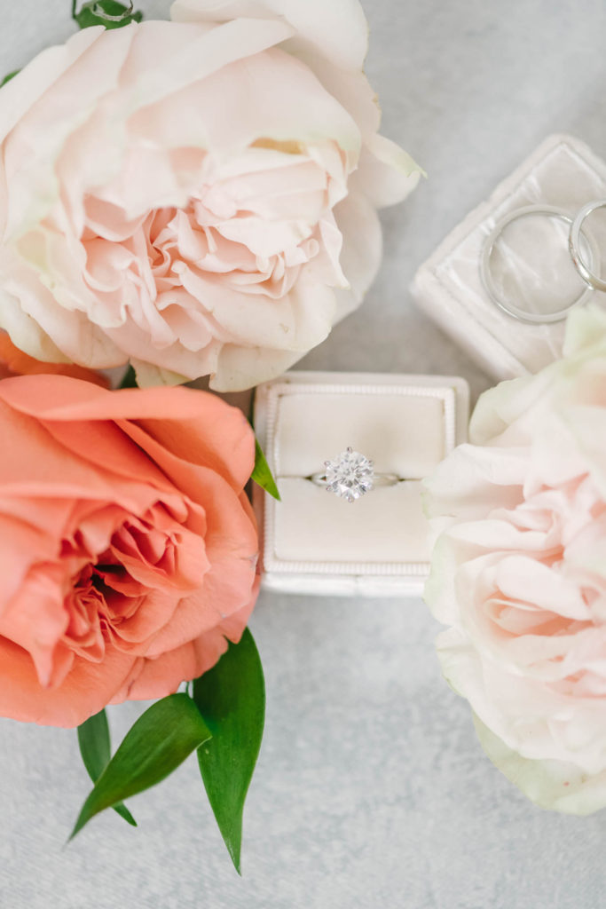 At an elopement in Wallisville Texas, a professional wedding photographer Christina Elliott Photography captures a flat-lay photo of a beautiful silver diamond ring surrounded by coral and white roses. wedding ring flat lay photo silver diamond wedding ring #christinaelliotphoto #christinaelliotphotography #christinaelliotelopements #elopementphotographer #wallisvillewedding #houstontexaswedding #houstonweddingphotographer #trinityfarmhouse #texaselopements #elopement #springwedding