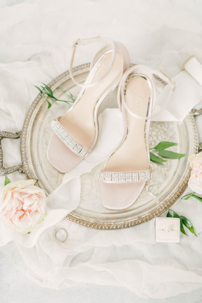 Christina Elliott Photography captures a stunning flat lay of the bride's wedding shoes along with the groom's ring and the bride's ring in Houston, Texas. wedding flat lay detail shot strappy wedding shoes elegant wedding shoe ideas #christinaelliotphoto #christinaelliotphotography #christinaelliotelopements #elopementphotographer #wallisvillewedding #houstontexaswedding #houstonweddingphotographer #trinityfarmhouse #texaselopements #elopement #springwedding