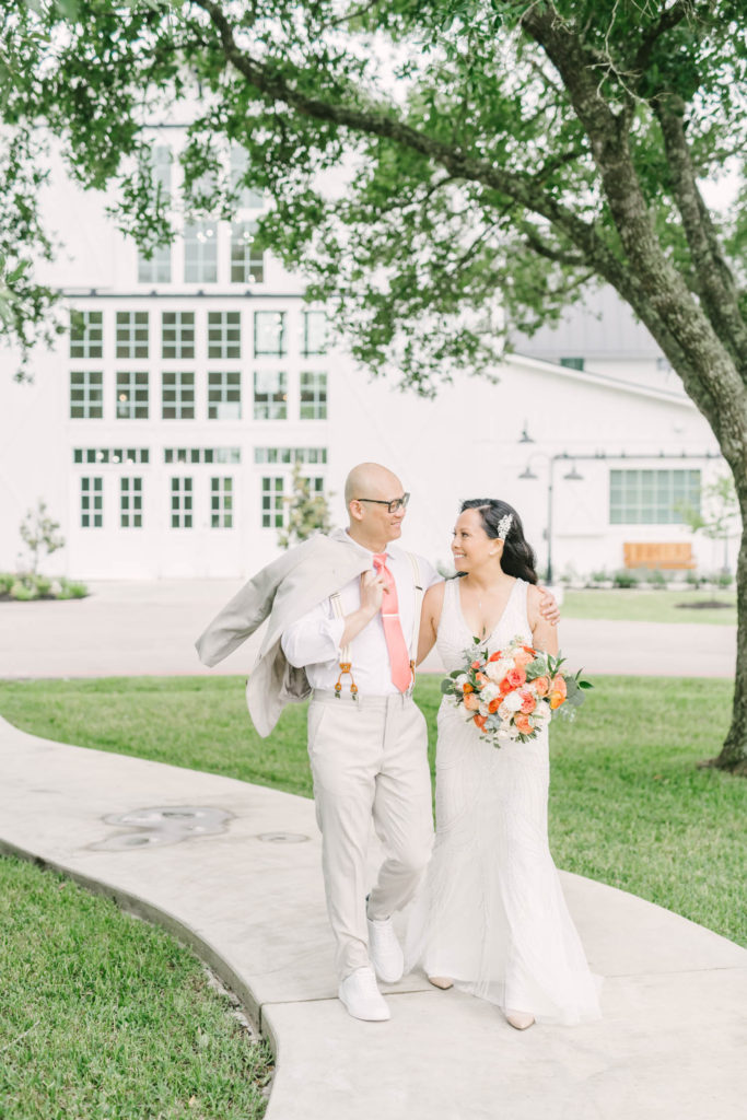 Groom with his suit jacket over his shoulder puts his arm around his bride and smiles lovingly at her as she returns the gaze at Trinity Farmhouse in Wallisville by Christina Elliott Photography. wedding send off elopement texas intimate wedding simple classy wedding #christinaelliotphoto #christinaelliotphotography #christinaelliotelopements #elopementphotographer #wallisvillewedding #houstontexaswedding #houstonweddingphotographer #trinityfarmhouse #texaselopements #elopement #springwedding