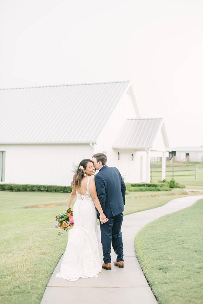 Perfect bride and groom in a white dress and navy suit with orange red and yellow flowers for a perfect summer farmhouse wedding in Texas by Christina Elliot Photography. how to dress for a summer wedding outfits for bride and groom poses for bride and groom classic wedding dress for bride classic suit for groom summer outfits for wedding white barn wedding #texasweddingphotographer #farmhousewedding #farmhouseweddinginspo #texasphotographer #farmhouseweddingdecor #texasweddinglocations